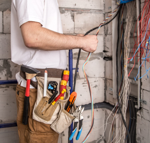 Electrician working near the Board with wires. Installation and connection of electrics. Professional with tools in hand.